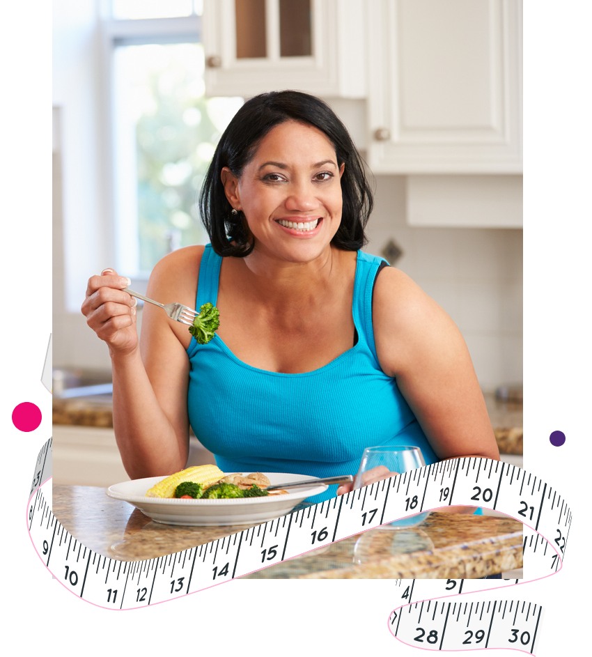 Smiling lady holding a folk with broccoli on it, with a plate of healthy food on the table